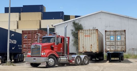 Red Kenworth truck driving away after offloading container